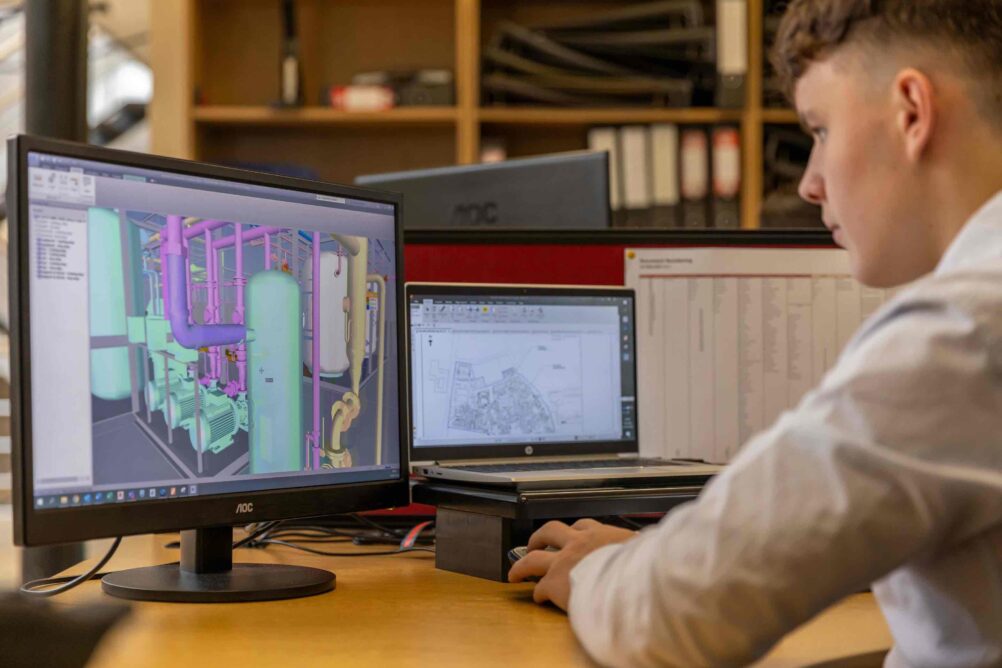 Man at a desk in front of two monitors displaying building software